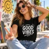 Good Vibes pozitív feliratos fekete streetwear póló fehér grafikával, mosolygó napszemüveges női modellen, városi gördeszkaparkban.