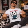Férfi fehér Michael Meowers pólóban, rajzolt fekete-fehér macskafigurával, késsel és sötétkék kezeslábasban.