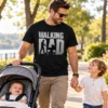 The Walking Dad vicces apuka póló fekete színben, szürke zombis paródiafelirattal, babakocsit toló és gyermekével sétáló apukán.