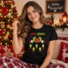 Fiatal nő fekete Anya Grinch karácsonyi pólóban, zöld Grinch-kezekkel, piros szívvel és családi figurákkal