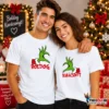 Fiatal pár fehér Grinch Hands Pólóban, összeillő zöld karácsonyi kézgrafikával és Boldog Karácsonyt felirattal.