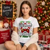 Fiatal nő fehér Ez a Karácsonyi Gamer pólóm pólóban, karácsonyi díszítésű gamer kontroller grafikával, ünnepi környezetben.