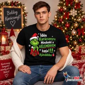 Fiatal férfi fekete Idén karácsonyra póló Grinch grafikával és „Idén karácsonyra mindenki a véleményem kapja ajándékba” felirattal, ünnepi környezetben.